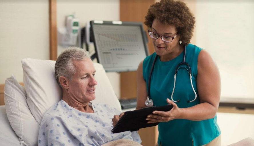 Teleurgent care image of healthcare professional with tablet consulting patient in hospital bed