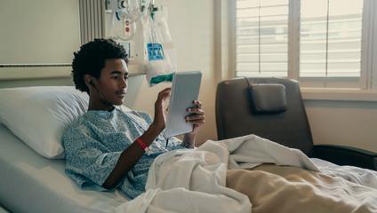On-demand telepsychiatry image of patient in hospital bed looking at tablet