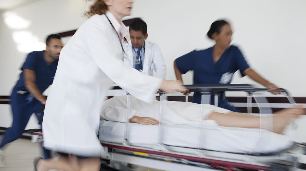 A team of medical professionals is rushing a patient on a stretcher through a hospital corridor.