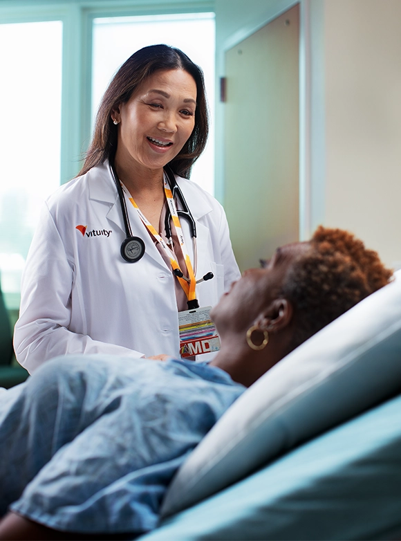 Female Vituity Medical Professional In White Labcoat Smiling While Consulting Patient In Hospital Be