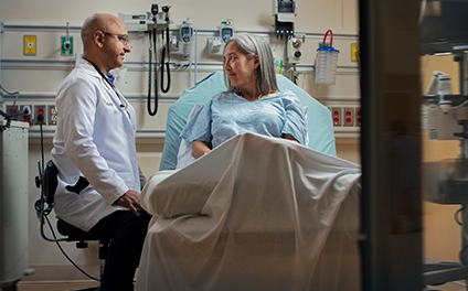 Male Vituity medical professional talking with patient in hospital bed