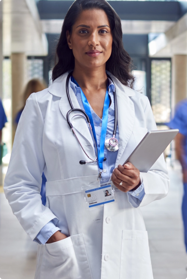 female doctor standing in hospital with clipboard and white lab coat and stethoscope around neck