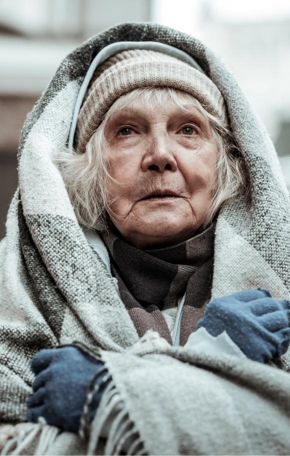 Image of elderly homeless woman wearing blanket and tattered clothing