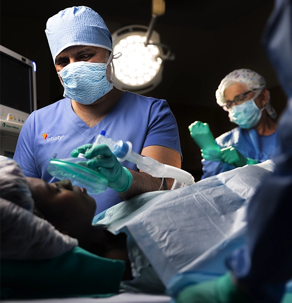 Vituity anesthesiologist wearing surgical mask and blue scrubs prepping patient