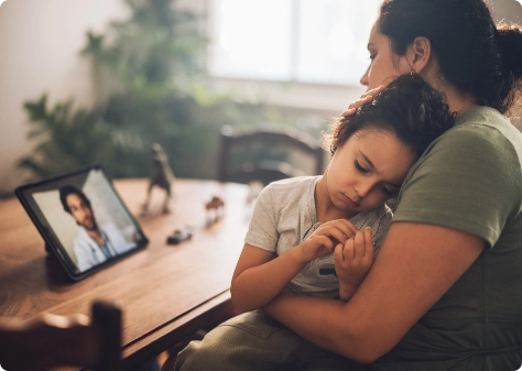 mother hugging daughter while on telehealth call with doctor on tablet screen
