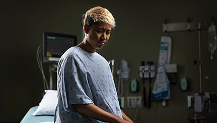 Concerned patient in hospital gown sitting on hospital bed