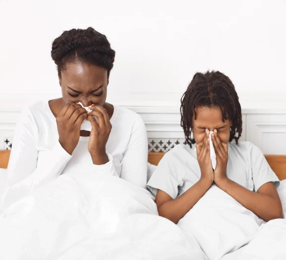 women and child sitting up in bed, sneezing before urgent care visit