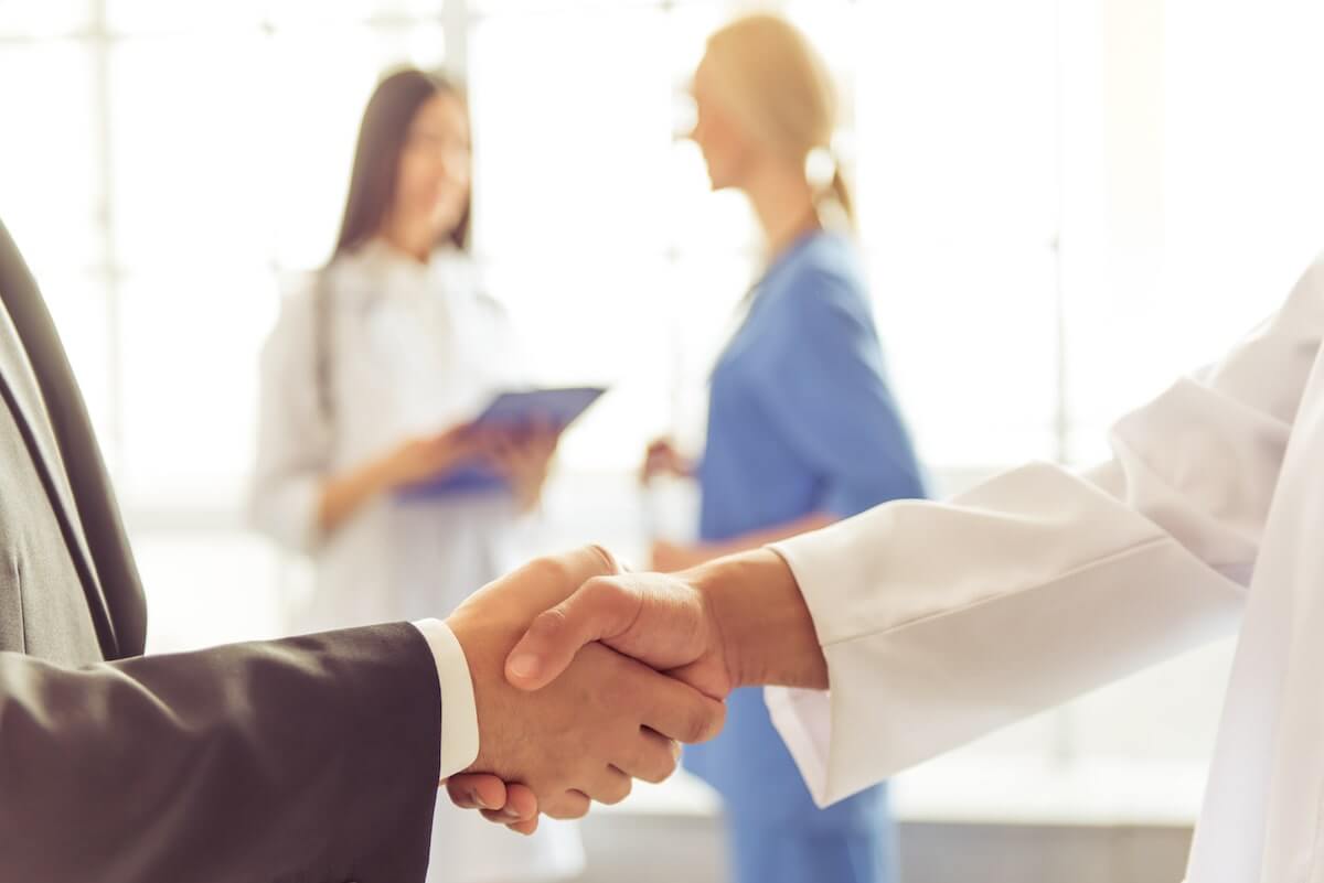 Doctor and hospital administrator shaking hands in hallway