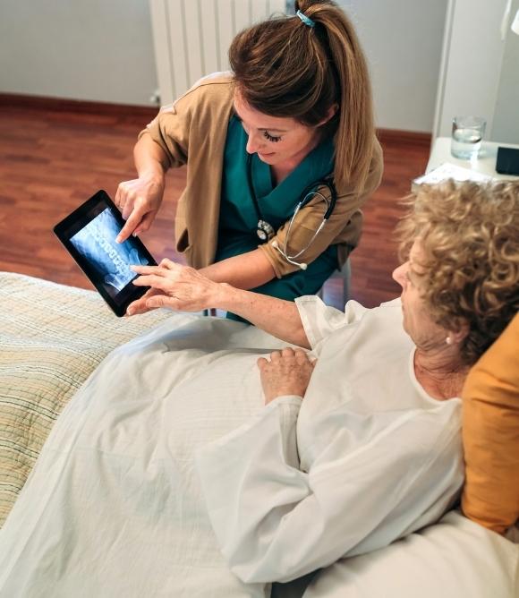 Image of hospital employee with patient holding tablet so patient can speak with teleskilled nursing staff member