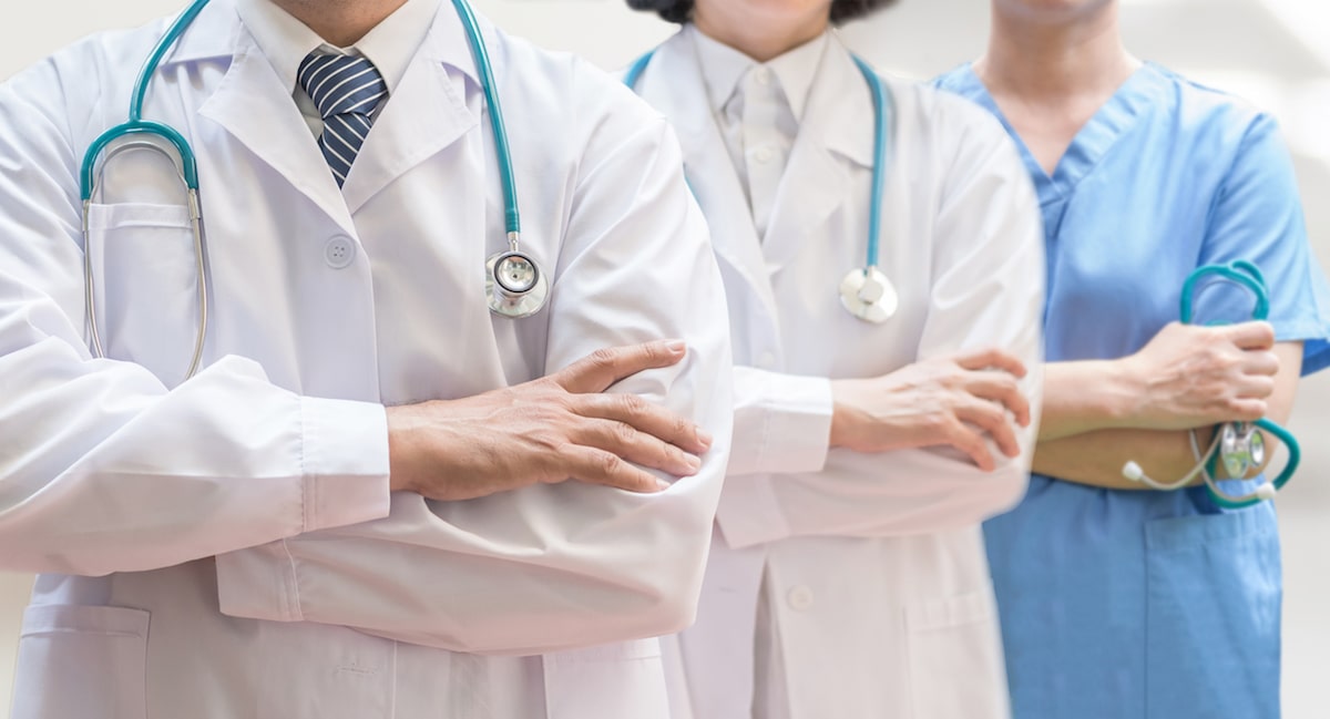 three doctors and nurses wearing stethoscopes standing elbow to elbow in a hospital hallway