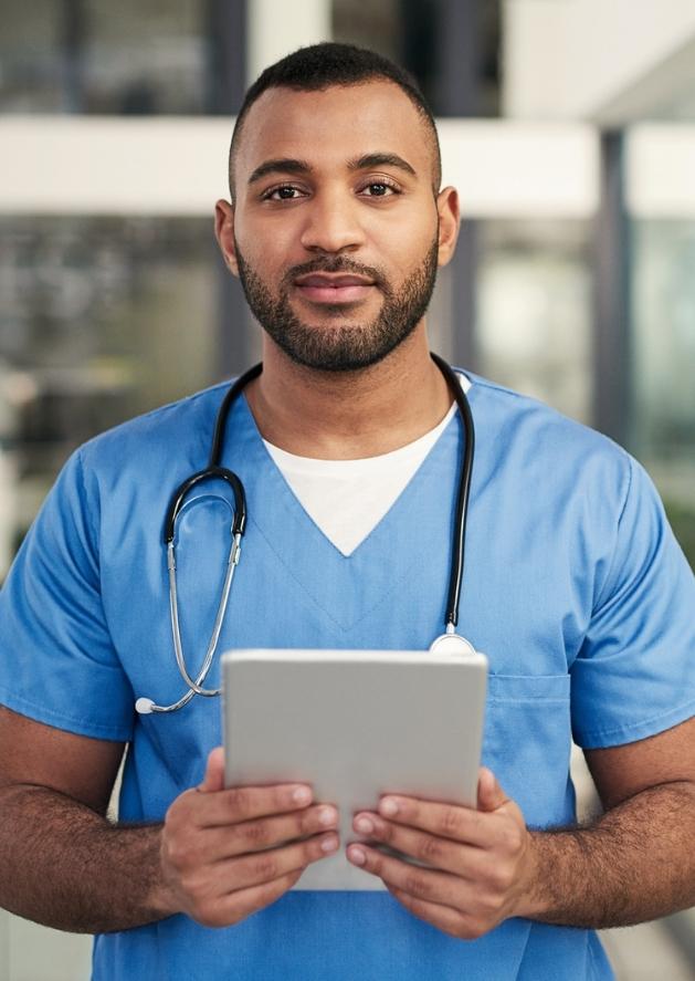 Resident physician in blue scrubs with a tablet in his hand and stethoscope around neck